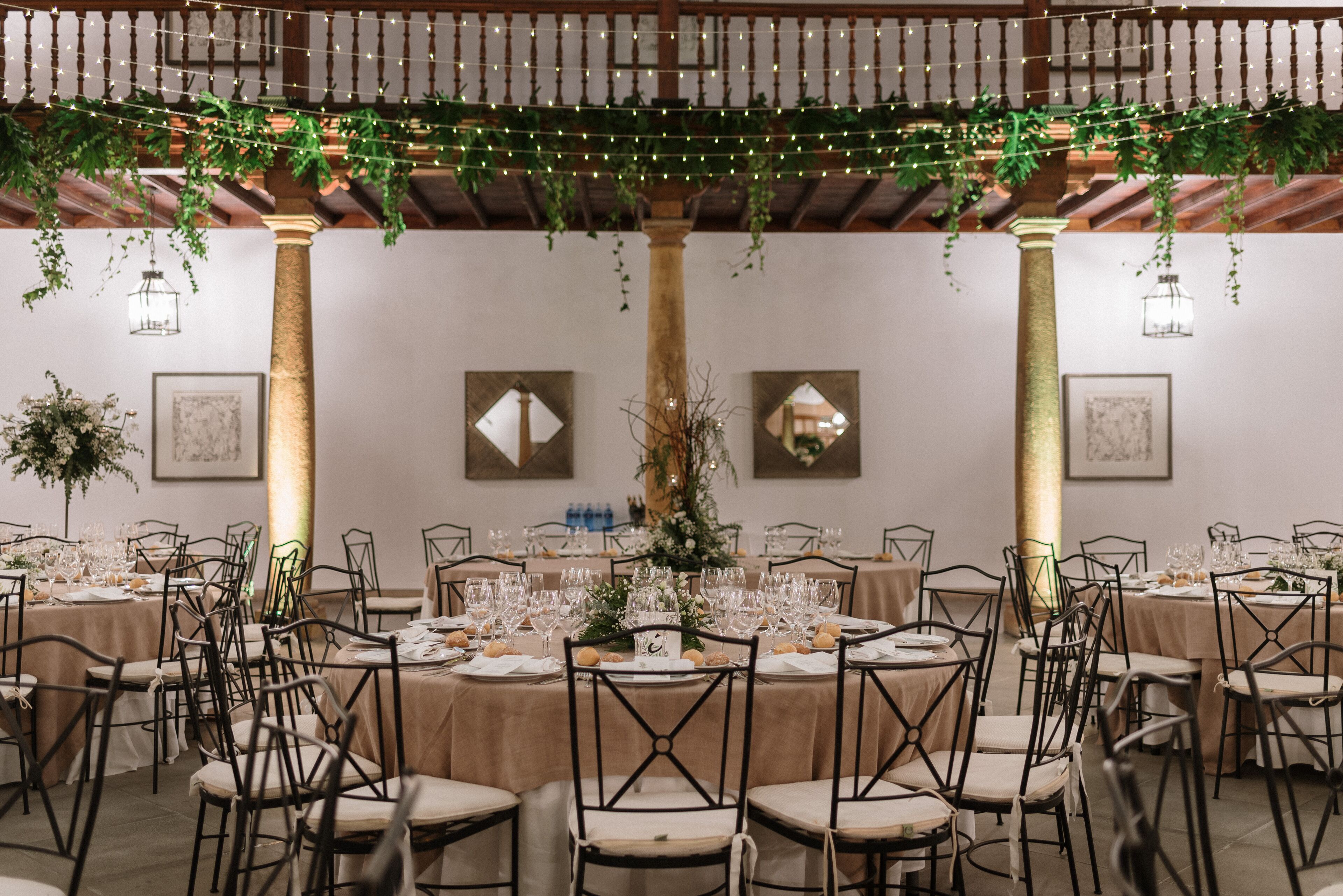 A banquet hall with round tables, chairs, and hanging greenery.