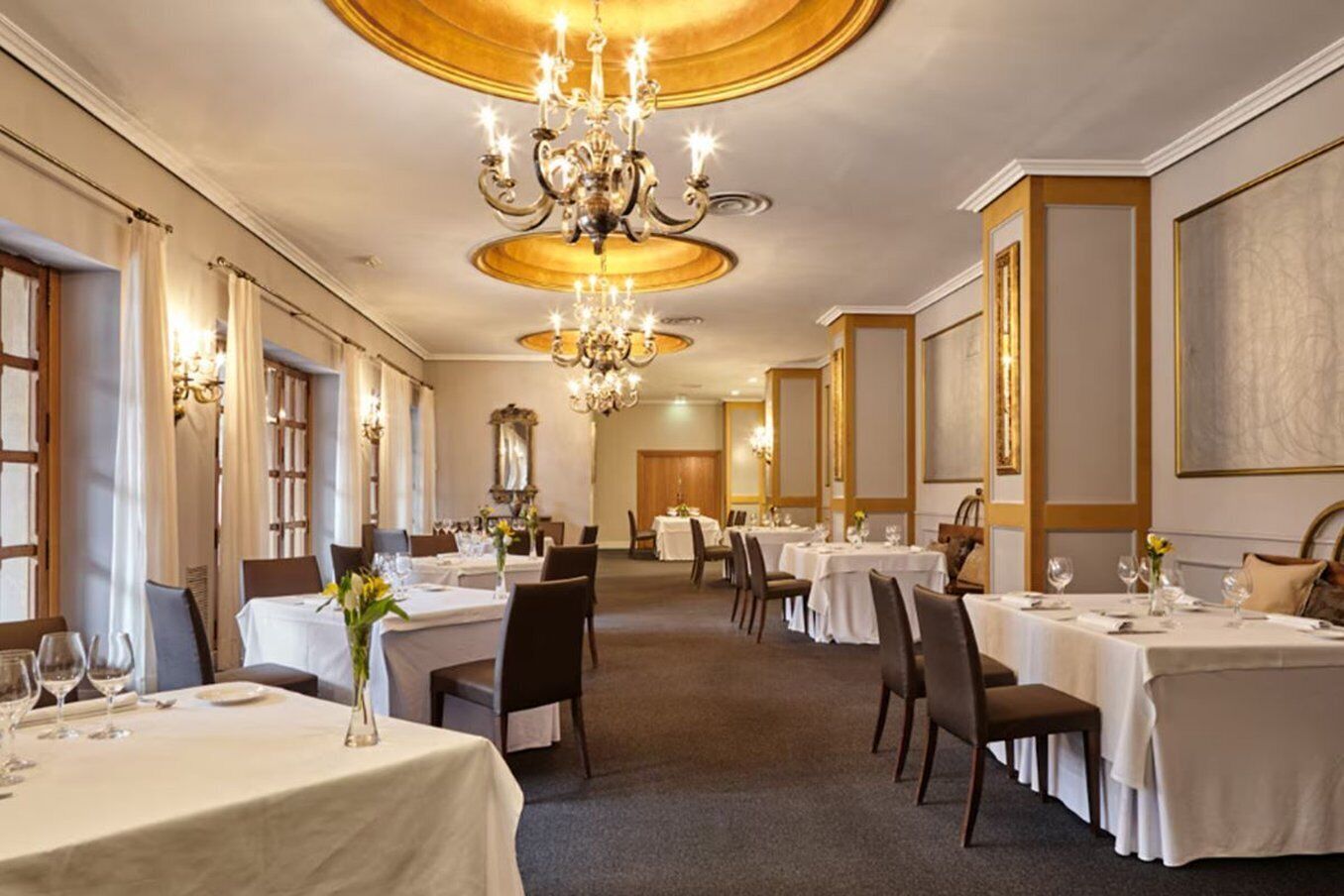 A formal dining room with multiple tables, chandeliers, and classic decor.