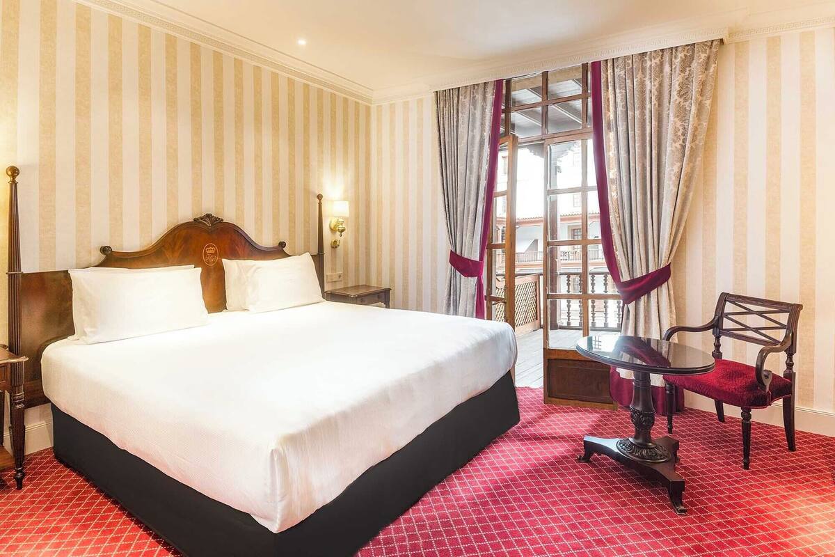 Ein Hotelzimmer mit einem großen Bett, einem Nachttisch, einem Sessel und Blick auf den Balkon.