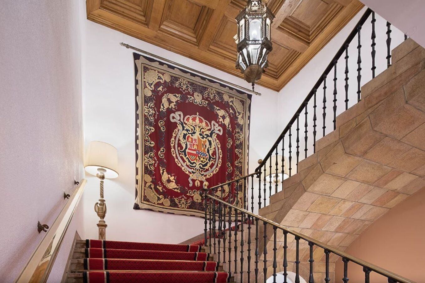 A grand staircase with red carpeted steps, a large ornate tapestry, and a classic chandelier.