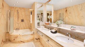 A luxurious bathroom with a large bathtub, two sinks, a walk-in shower, and marble walls.
