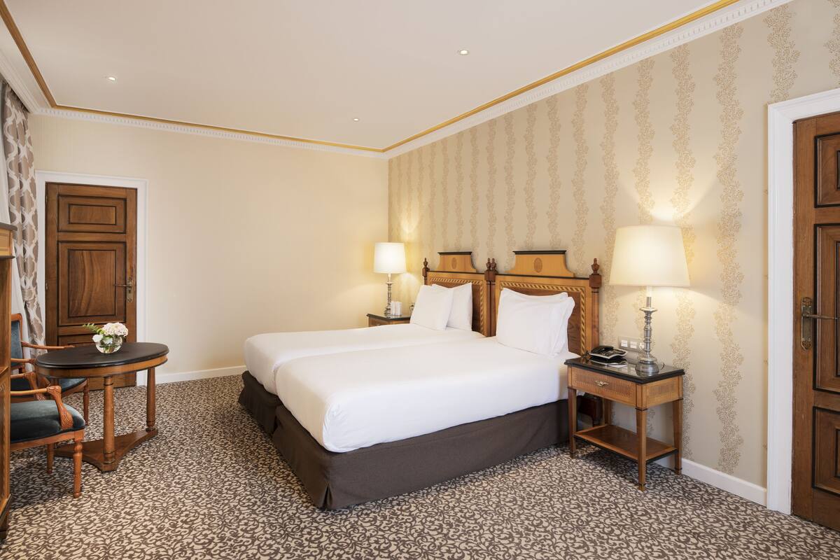 Ein Hotelzimmer mit einem großen Bett, zwei Nachttischen mit Lampen, einem kleinen Tisch mit einer Vase und einem Sessel.