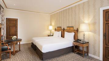 Habitación de hotel con una cama grande, dos mesitas de noche con lámparas, una pequeña mesa con un jarrón y una silla.