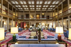 Eine geräumige Lobby mit hoher Decke, aufwendigen Säulen und einer zentralen Sitzecke mit Sofas und Tischen.