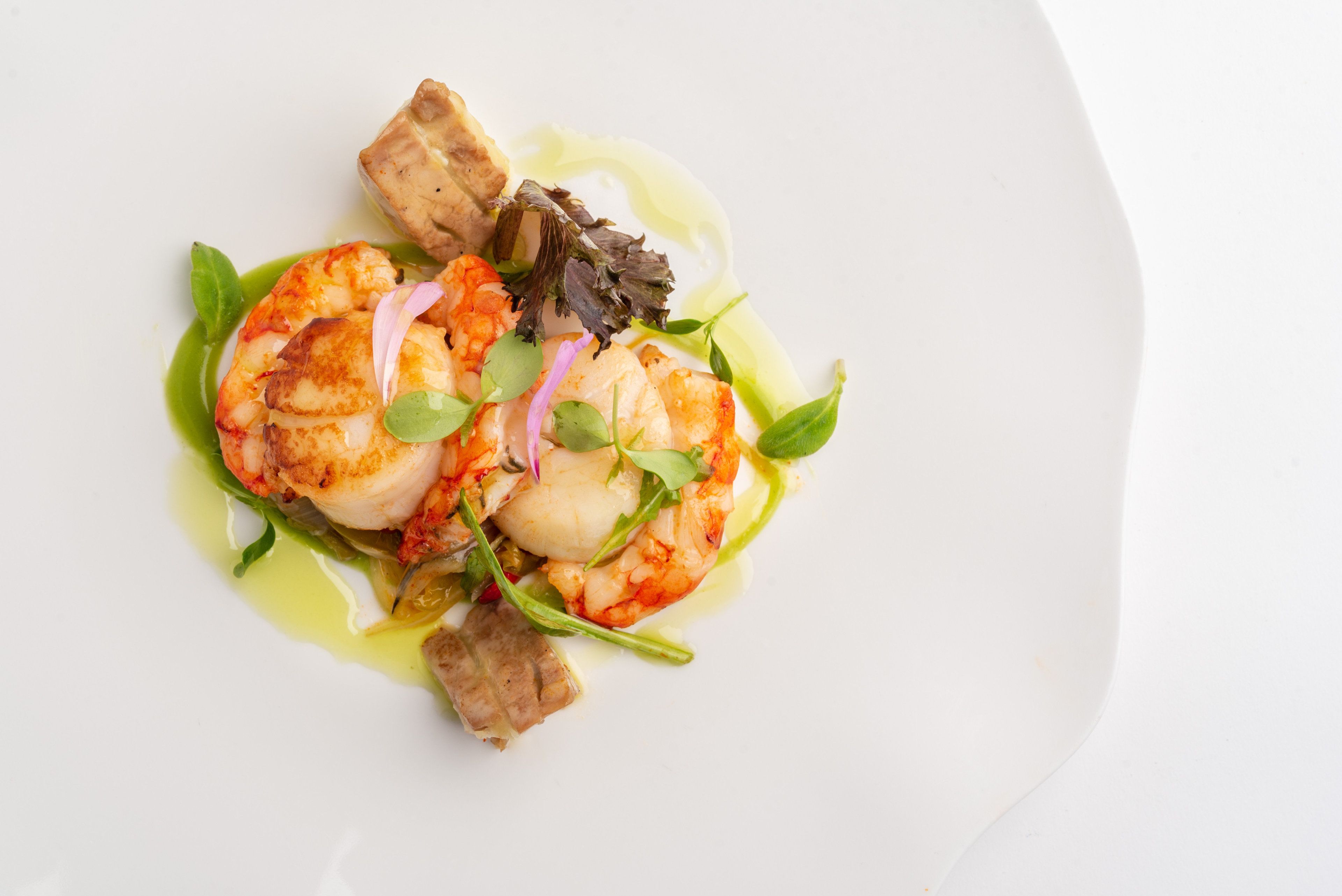 A white plate with a seafood dish consisting of shrimp, scallops, and a green sauce.