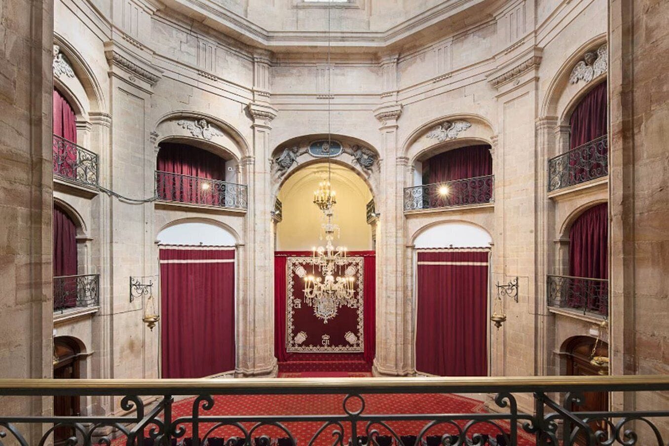 A grand hall with a red carpet, ornate chandeliers, and red curtains.