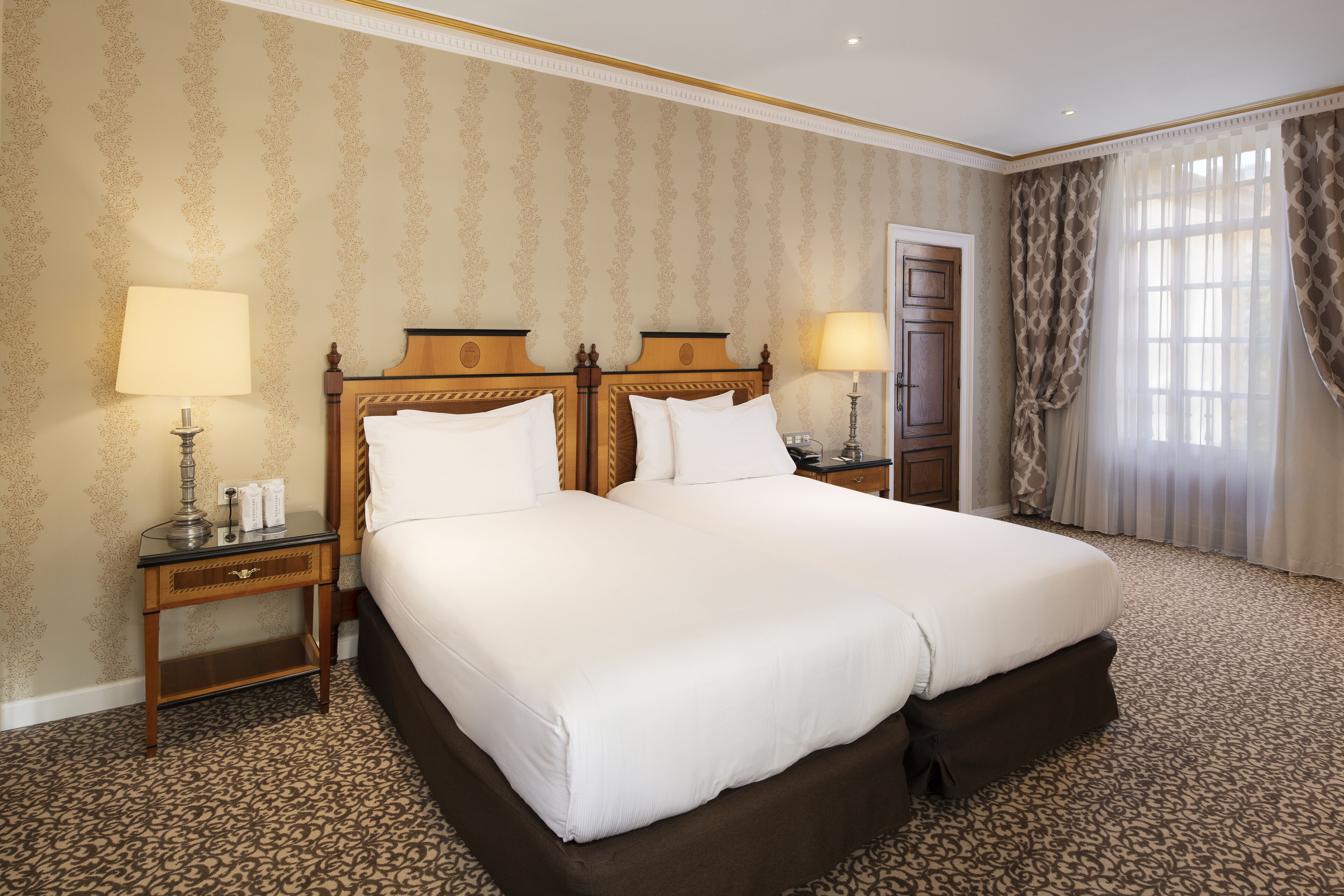 Una habitación de hotel con una cama grande, dos mesitas de noche con lámparas, un armario y una ventana con cortinas.