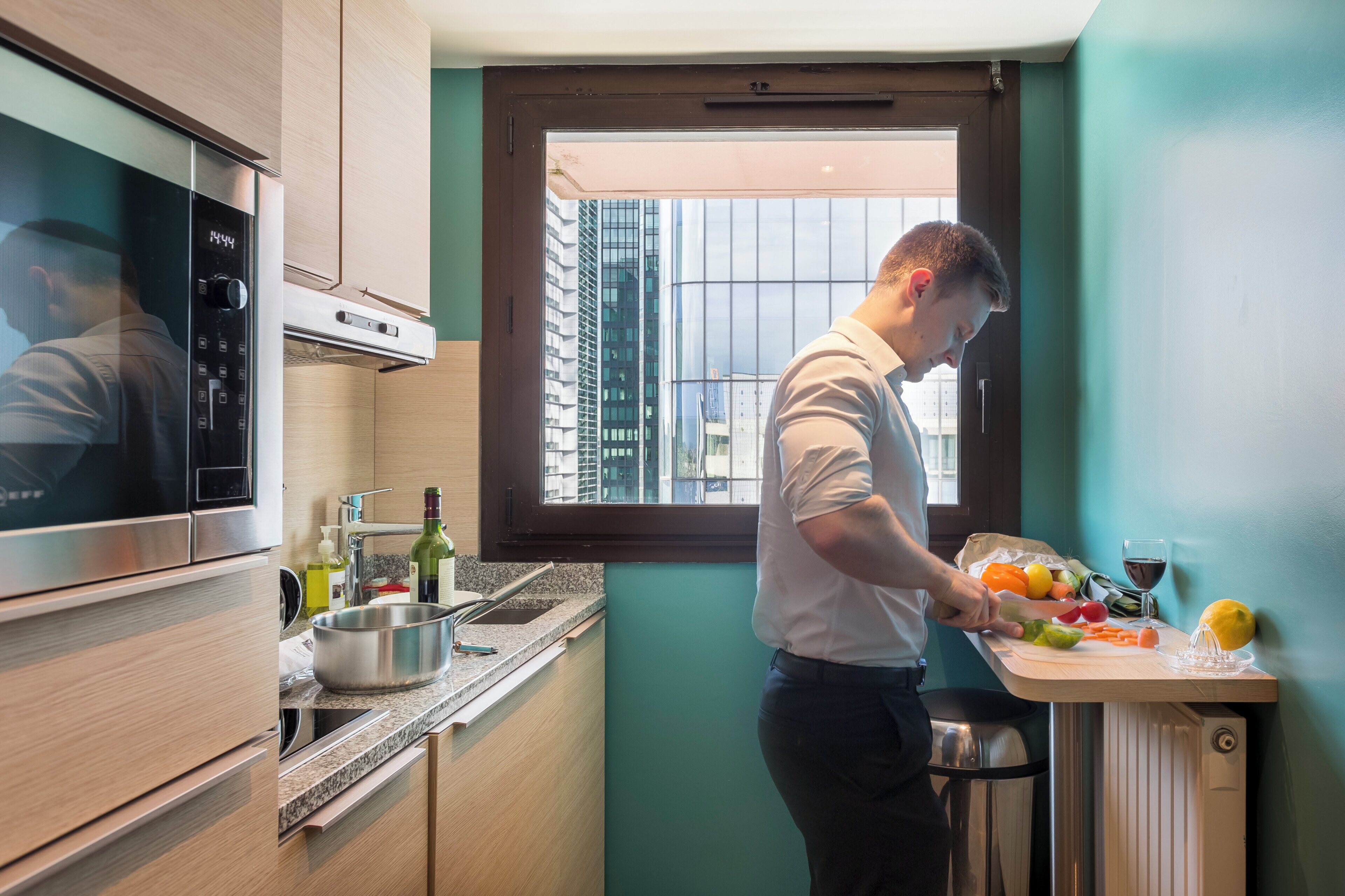 Una cocina compacta con electrodomésticos modernos, un ventanal con vistas a edificios y una encimera con productos frescos.