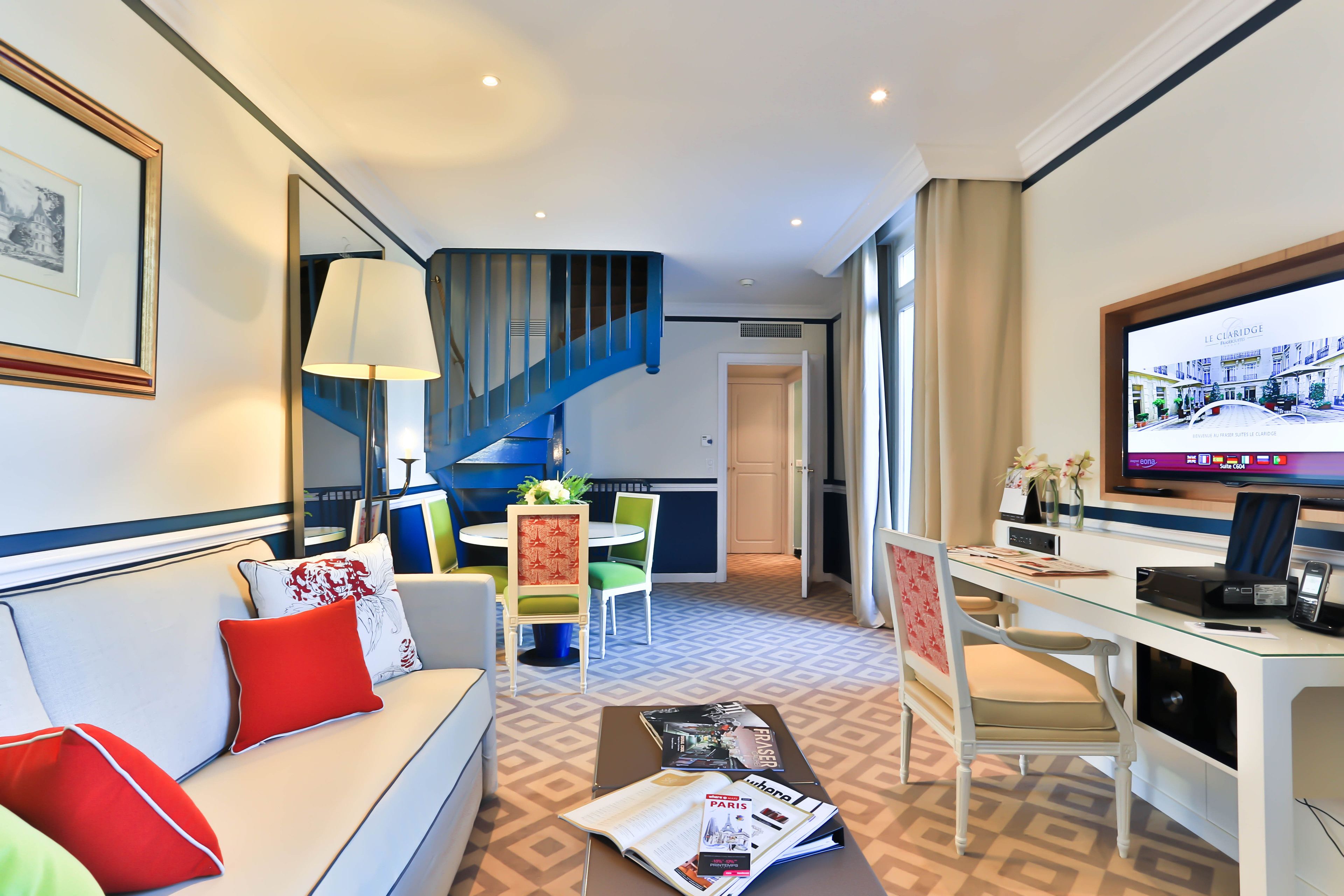 A hotel room with a sofa, dining table, chairs, a TV, and a staircase.
