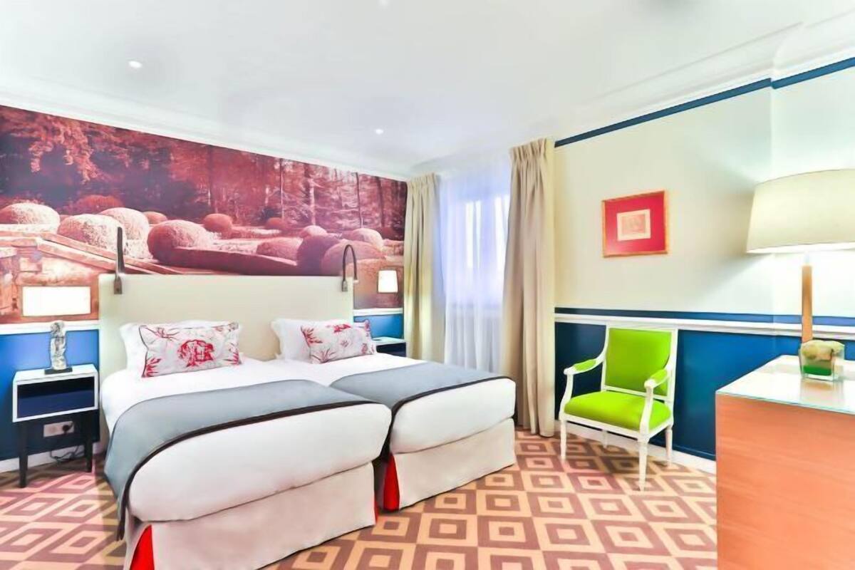 A hotel room with a large bed, a desk, a chair, and a wall mural.