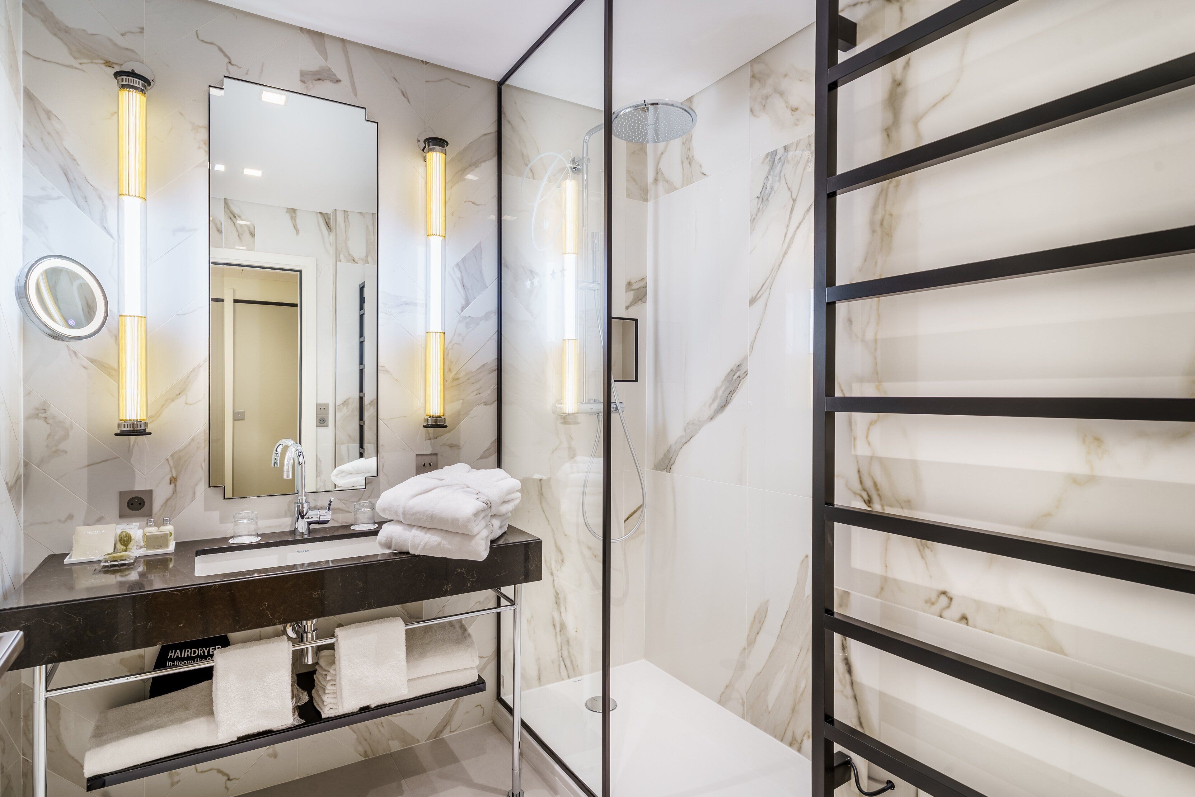 A modern bathroom with a marble wall, a large mirror, a dark countertop, and a glass shower enclosure.