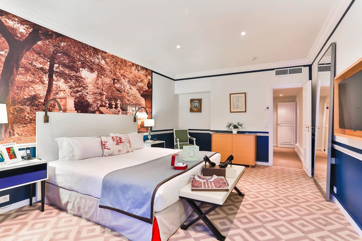 A hotel room with a large bed, a desk with a computer, a chair, and a TV.