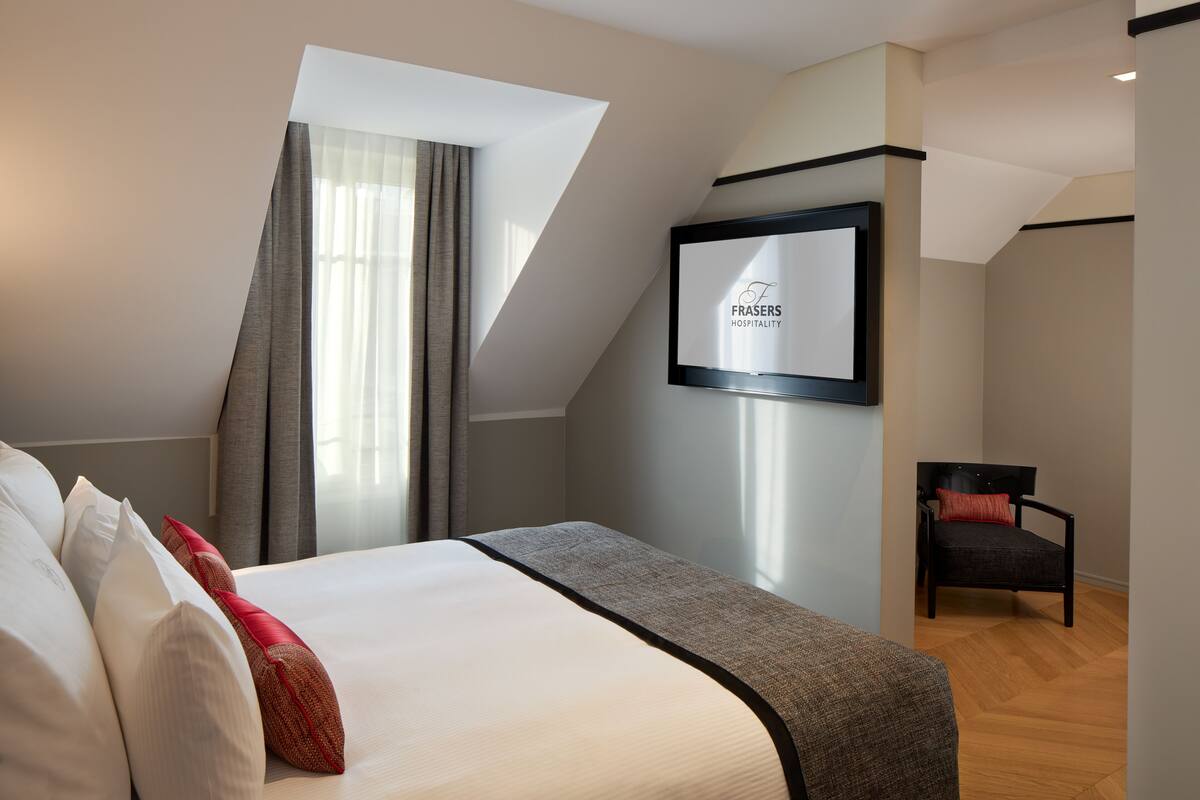 A hotel room with a bed, a chair, a framed sign on the wall, and a window with curtains.