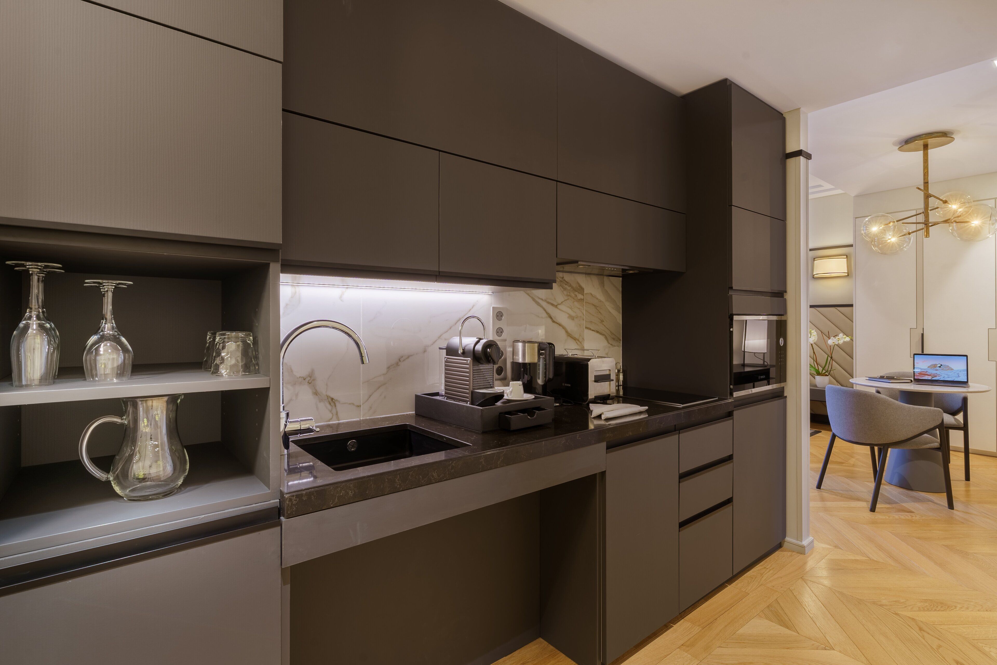 A modern kitchen with dark cabinetry, a marble backsplash, and a built-in coffee maker.