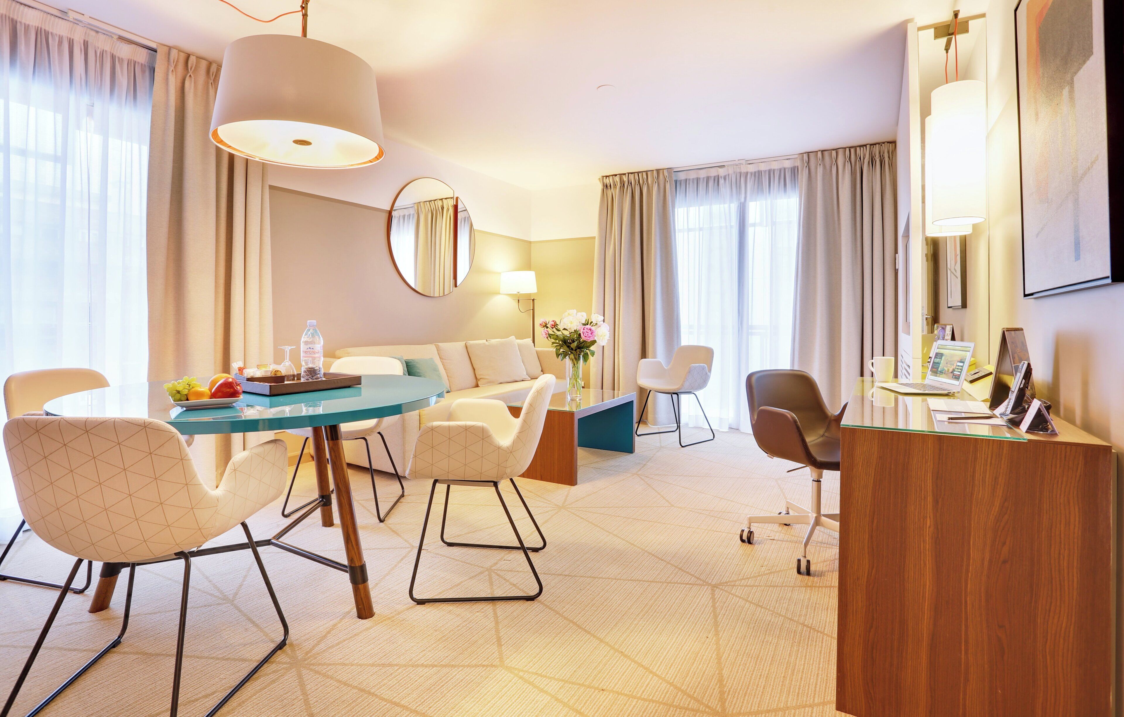 Habitación de hotel con zona de comedor, escritorio con computadora, silla y un espejo grande.