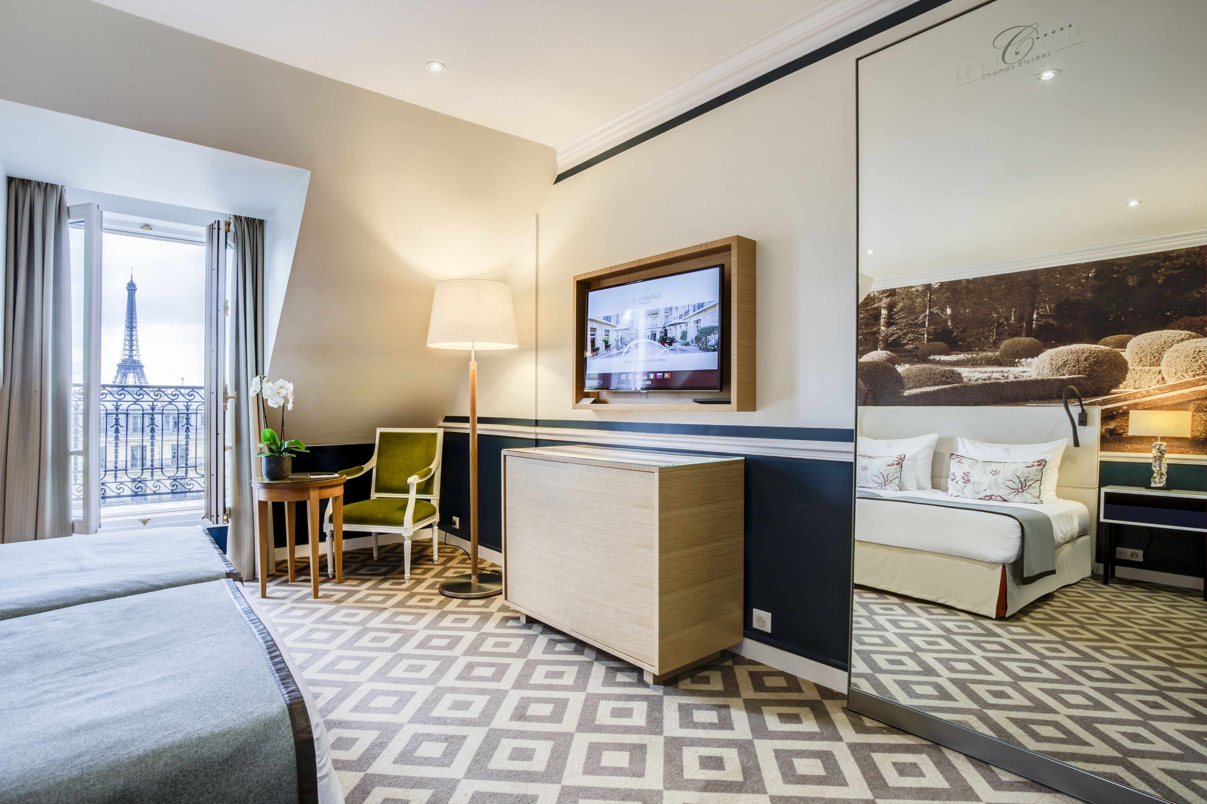 A hotel room with a bed, a desk, a chair, a TV, and a view of the Eiffel Tower.