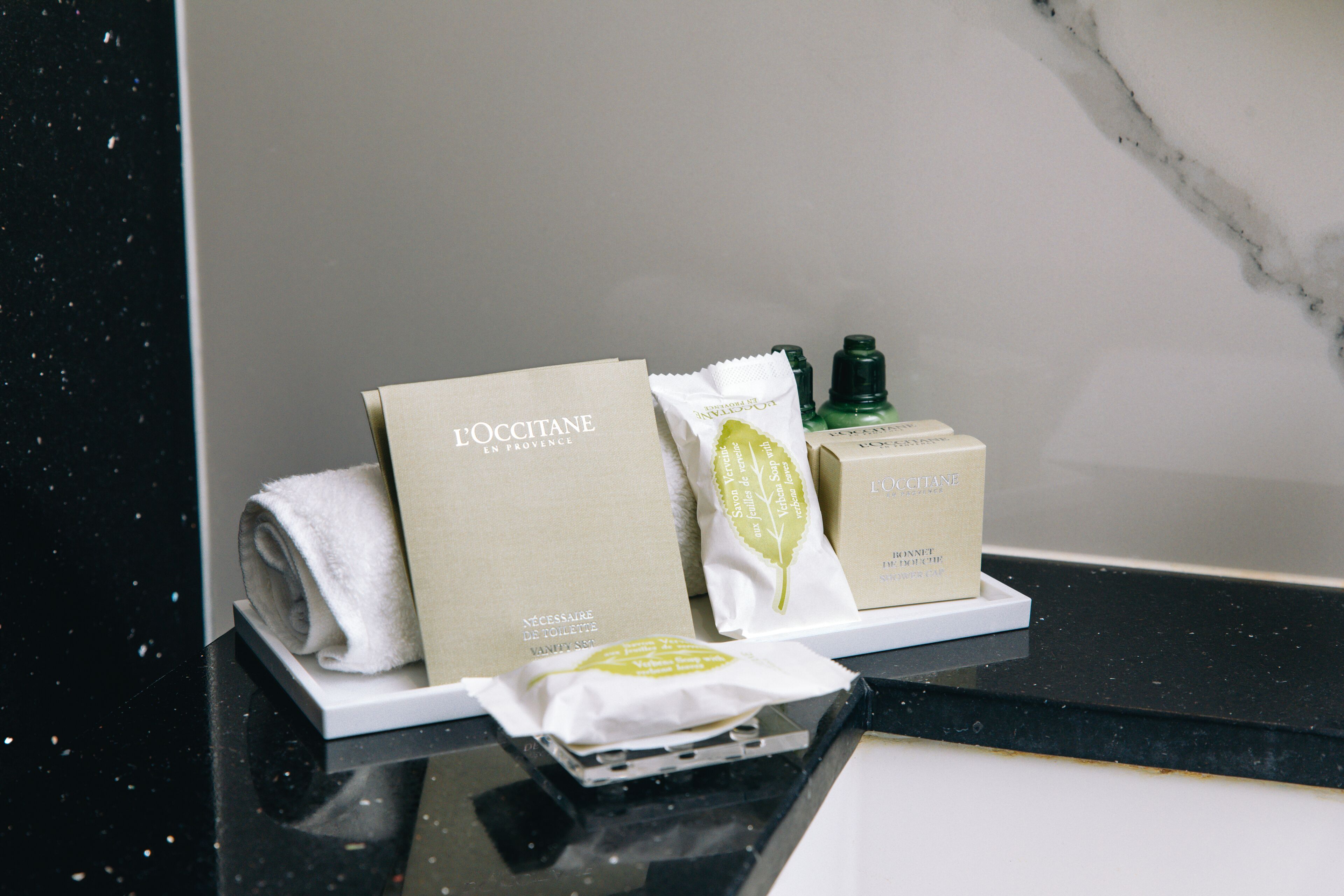 A bathroom counter with toiletries including a towel, a white box, a green bottle, and a white packet.