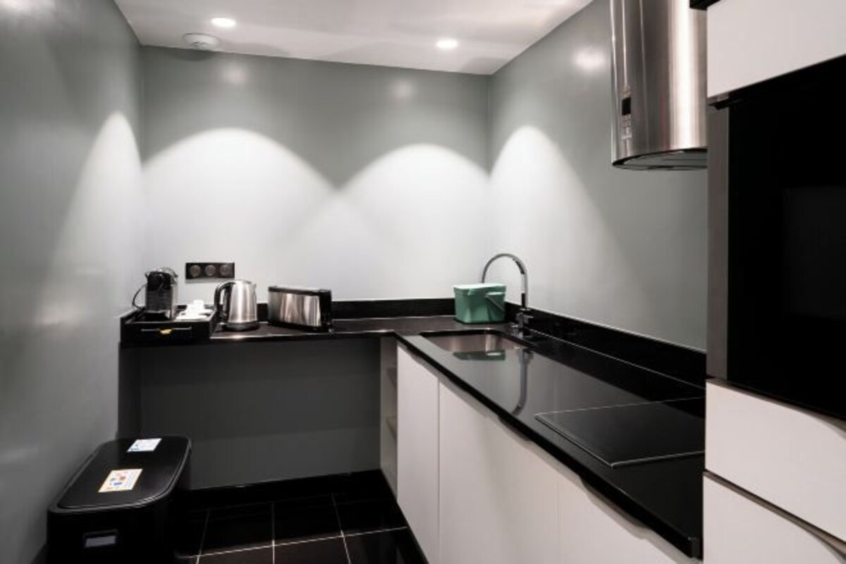 Una cocina compacta con encimera negra, electrodomésticos de acero inoxidable y un lavabo.