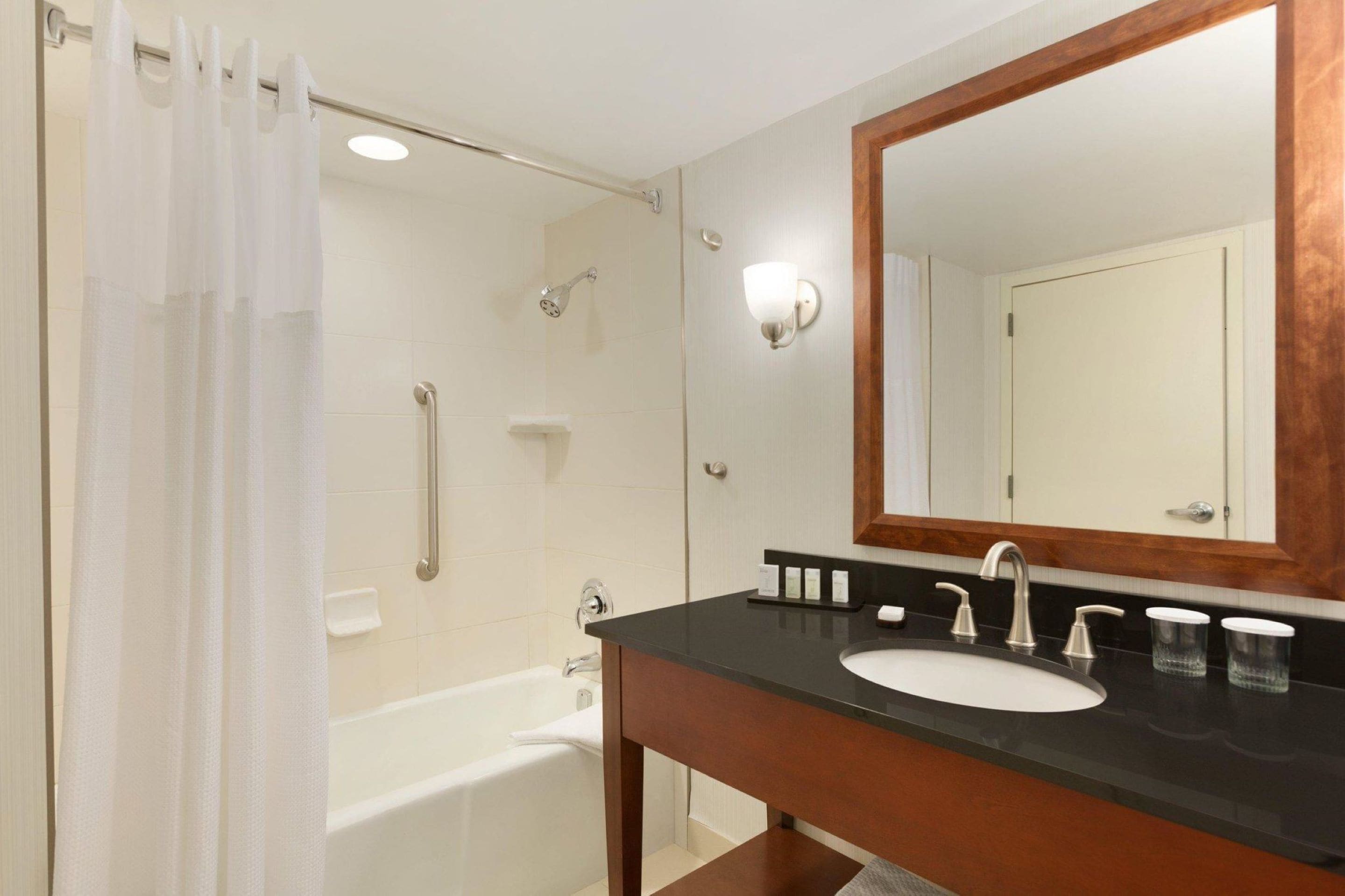 Un baño con bañera, ducha, lavamanos con espejo y toallero.