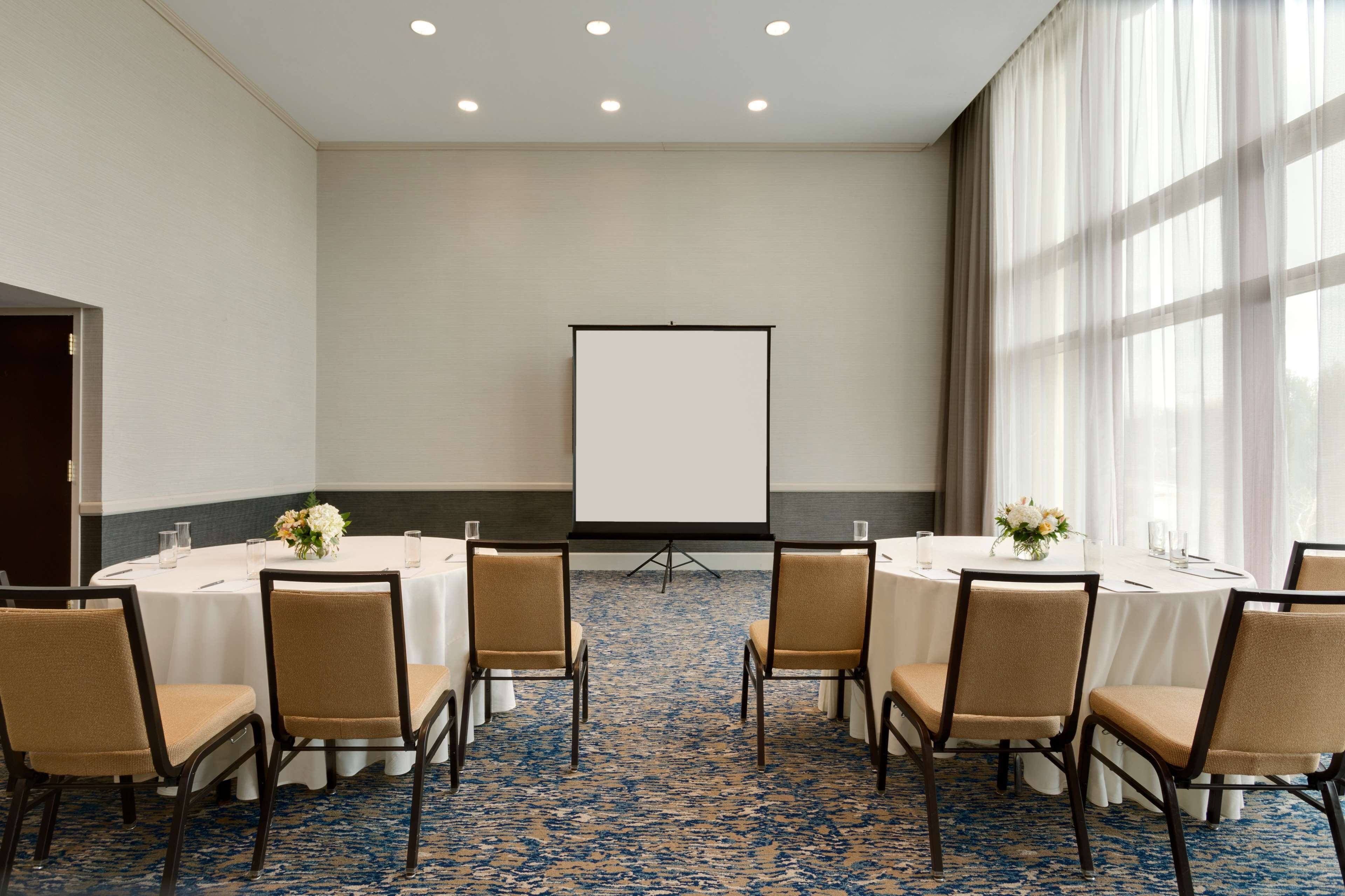Un salón de conferencias con una pizarra, mesas redondas y sillas.