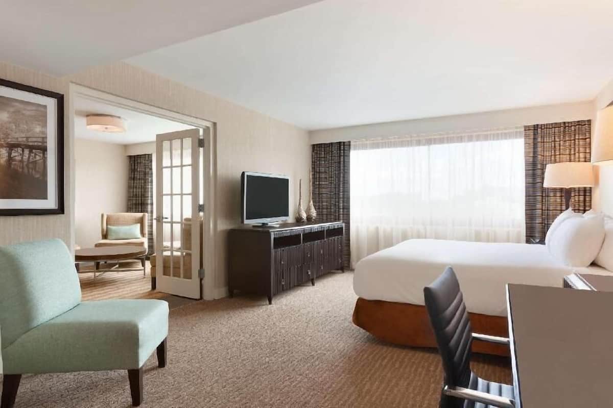 A hotel room with a bed, a desk, a chair, a television, and a door leading to another room.