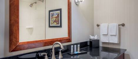 Une salle de bain avec un lavabo noir, un grand miroir, un porte-serviettes avec deux serviettes et un tableau encadré au mur.