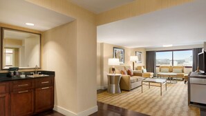 A hotel room with a wooden cabinet, a sofa, a coffee table, and a TV. - Embassy Suites by Hilton Boston Waltham (Waltham)