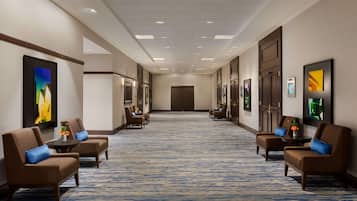 A hotel lobby with a long corridor, seating areas with brown chairs and blue cushions, and framed artwork on the walls.