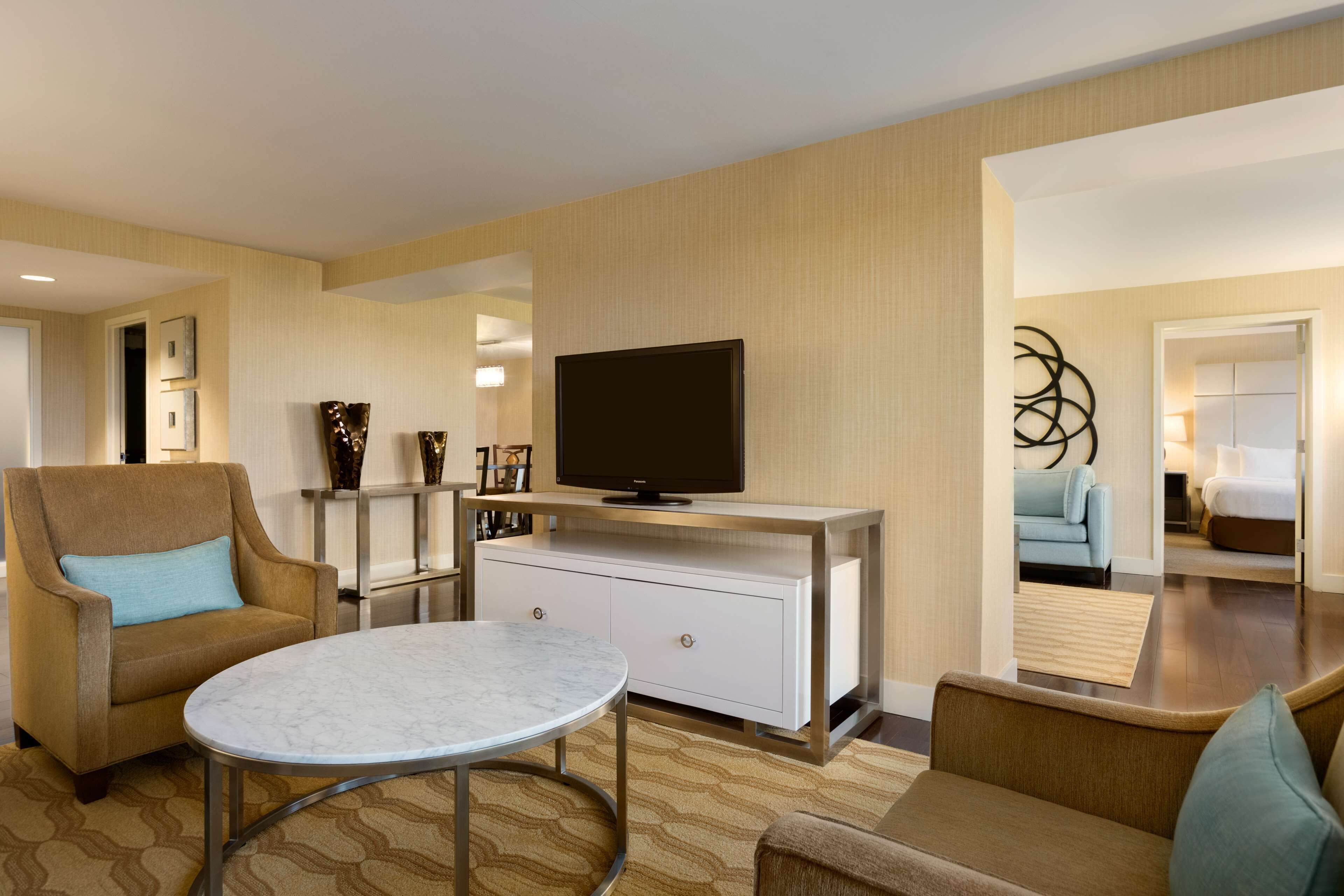 Una habitación de hotel moderna con un sofá, un televisor en un mueble, una mesa redonda y un adorno en la pared.