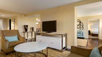 Una habitación de hotel moderna con un sofá, un televisor en un mueble, una mesa redonda y un adorno en la pared.