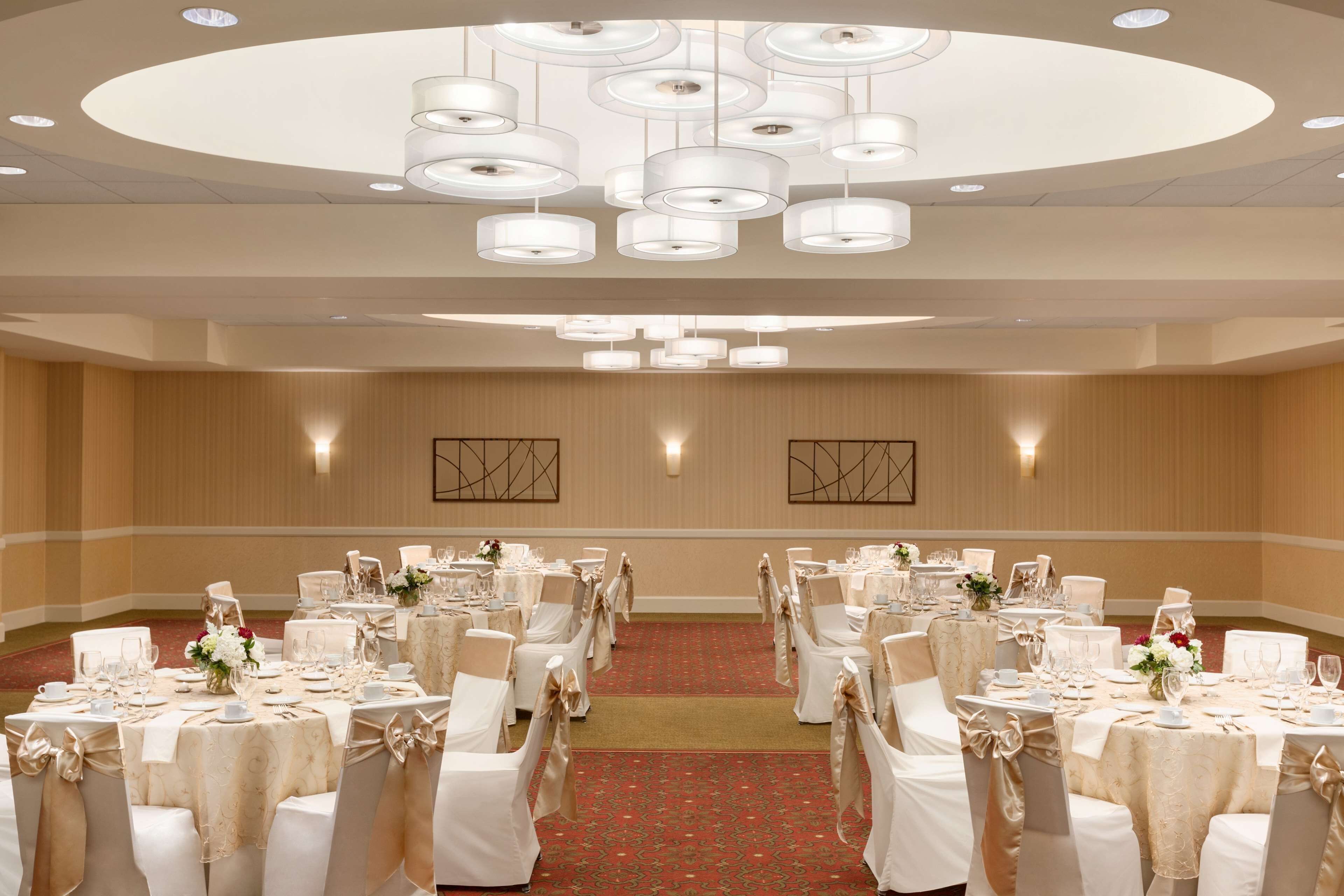 A banquet hall with round tables, white chairs, and chandeliers.