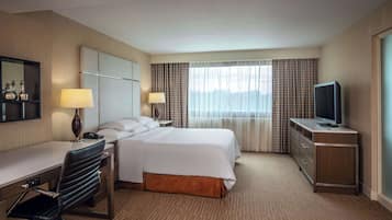 Una habitación de hotel con cama, escritorio, silla, televisor y ventana con cortinas.