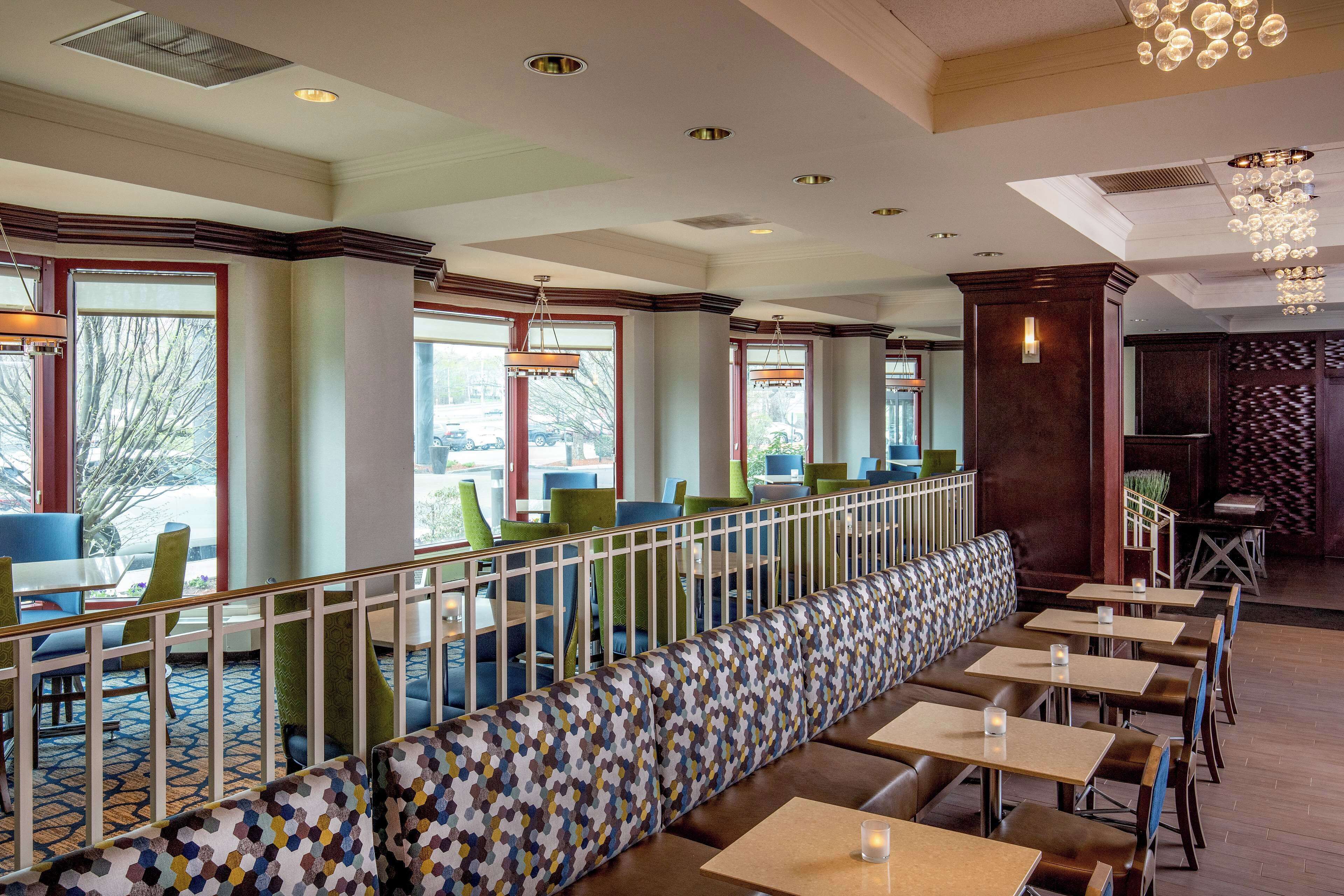 A restaurant with a long bench seating area, tables, and a railing.