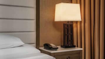 A neatly made bed with white linens, a bedside table with a lamp, a telephone, and a wooden nightstand.