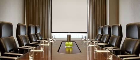A conference room with a long table, black leather chairs, and a projector screen at the front.