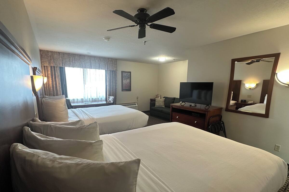 A hotel room with two beds, a ceiling fan, a TV, a dresser, and a mirror.