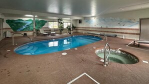 An indoor swimming pool with a mural of a landscape on the walls, a seating area with chairs, and a small hot tub. - Alpine Inn & Suites (Gunnison)