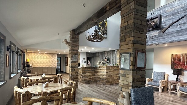 A restaurant interior with rustic wooden tables and chairs, stone pillars, and a fireplace. - Alpine Inn & Suites (Gunnison)
