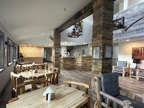A restaurant interior with rustic wooden tables and chairs, stone pillars, and a fireplace.