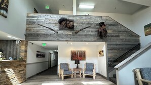 A lobby with a wooden staircase, two armchairs, a small table, and a wall-mounted fireplace. - Alpine Inn & Suites (Gunnison)