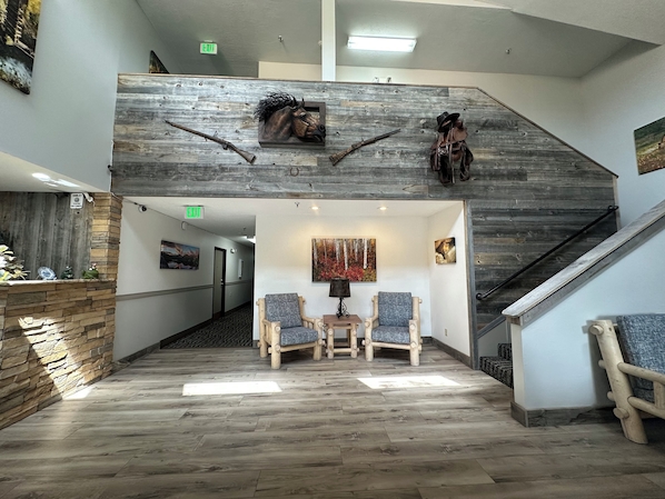 A lobby with a wooden staircase, two armchairs, a small table, and a wall-mounted fireplace.