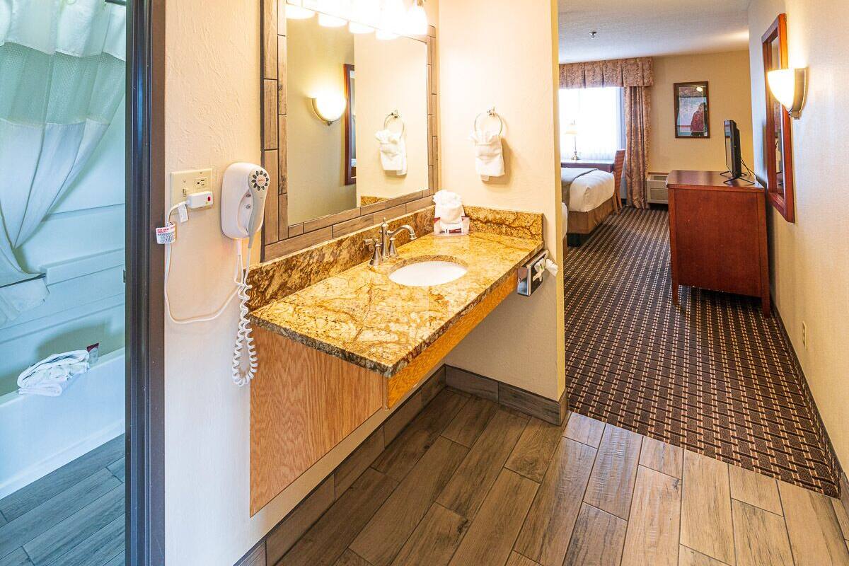 A hotel bathroom with a marble sink, a large mirror, and a shower area.