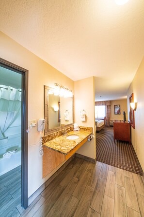 Baño de hotel con lavamanos de mármol, un espejo grande y zona de ducha.