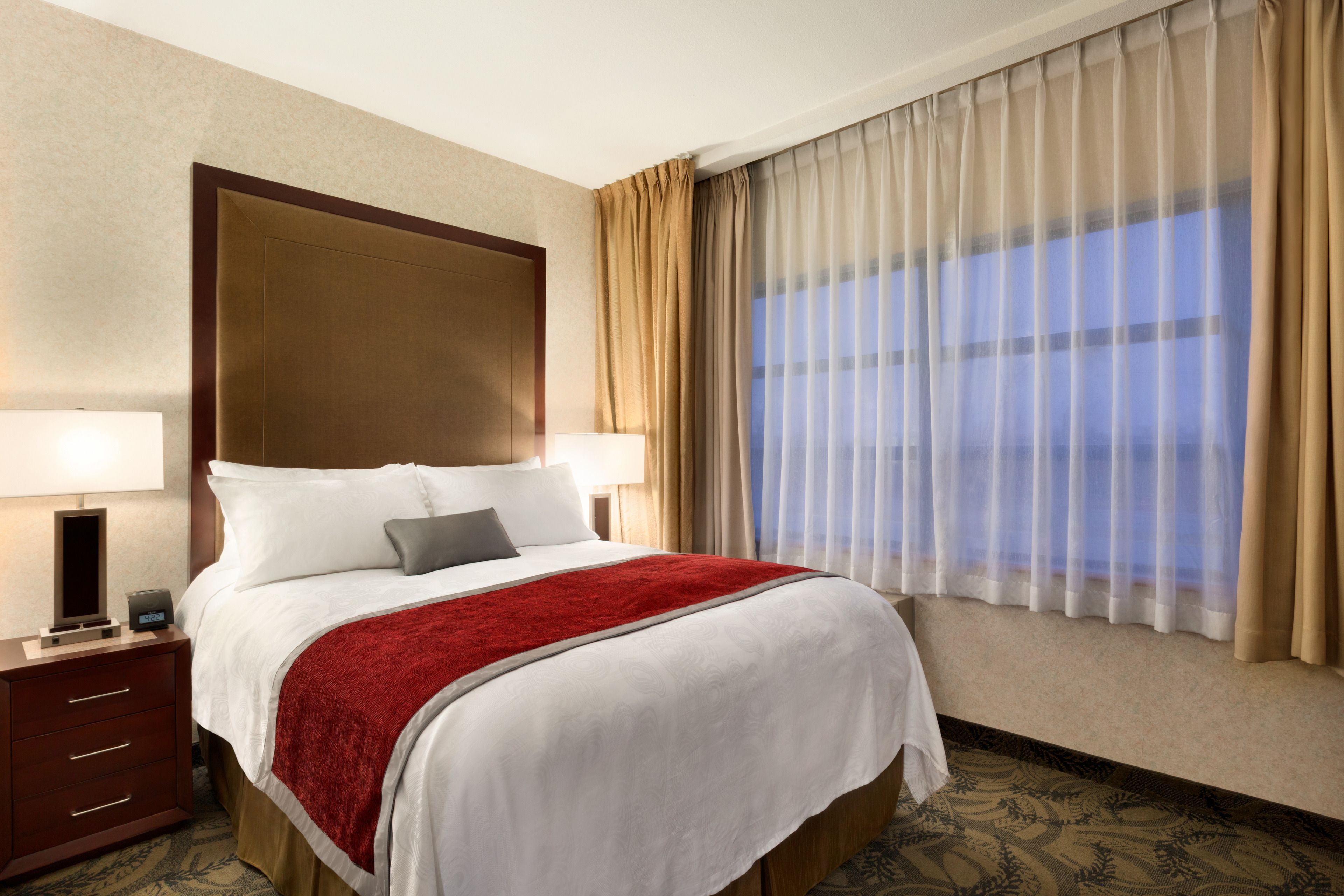 Une chambre d’hôtel avec un grand lit, une table de chevet, une lampe et une fenêtre avec des rideaux.
