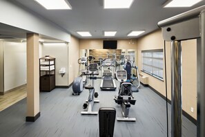 Une salle de sport moderne équipée de divers appareils d’exercice, d’un grand miroir et d’un téléviseur fixé au mur.