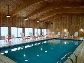 Une piscine intérieure avec des murs en bois, de nombreux fauteuils et des luminaires au plafond.