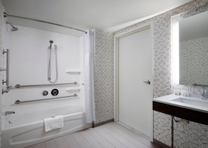 Une salle de bain moderne dotée d’une douche à l’italienne, de barres d’appui, d’une baignoire et d’un lavabo avec un miroir.