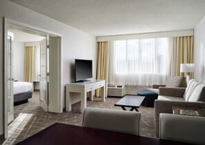 A hotel room with a bed, a desk with a television, a seating area with a sofa and armchairs, and a large window with curtains. - Holiday Inn & Suites Marlborough by IHG (Marlborough)