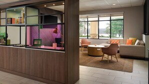 A modern hotel lobby with a reception desk, seating area, and large windows offering a view of the outdoors.