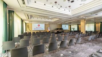 Un salón de conferencias de hotel con filas de sillas, un atril y un coche estacionado afuera.